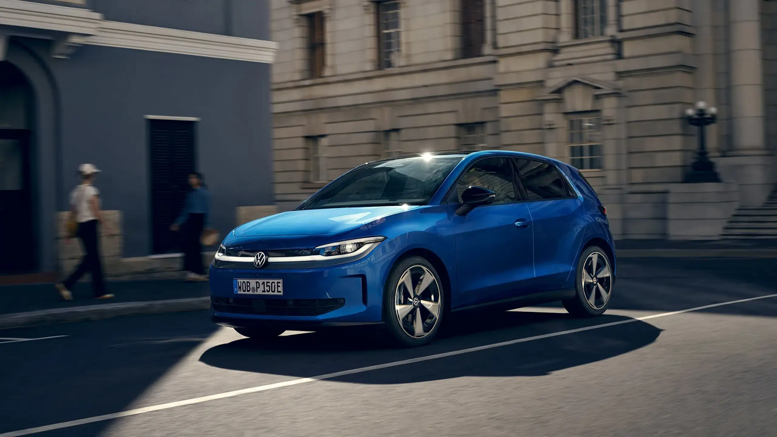 Blå Volkswagen ID. Polo set skråt forfra, der kører på en byvej foran klassiske bygninger.