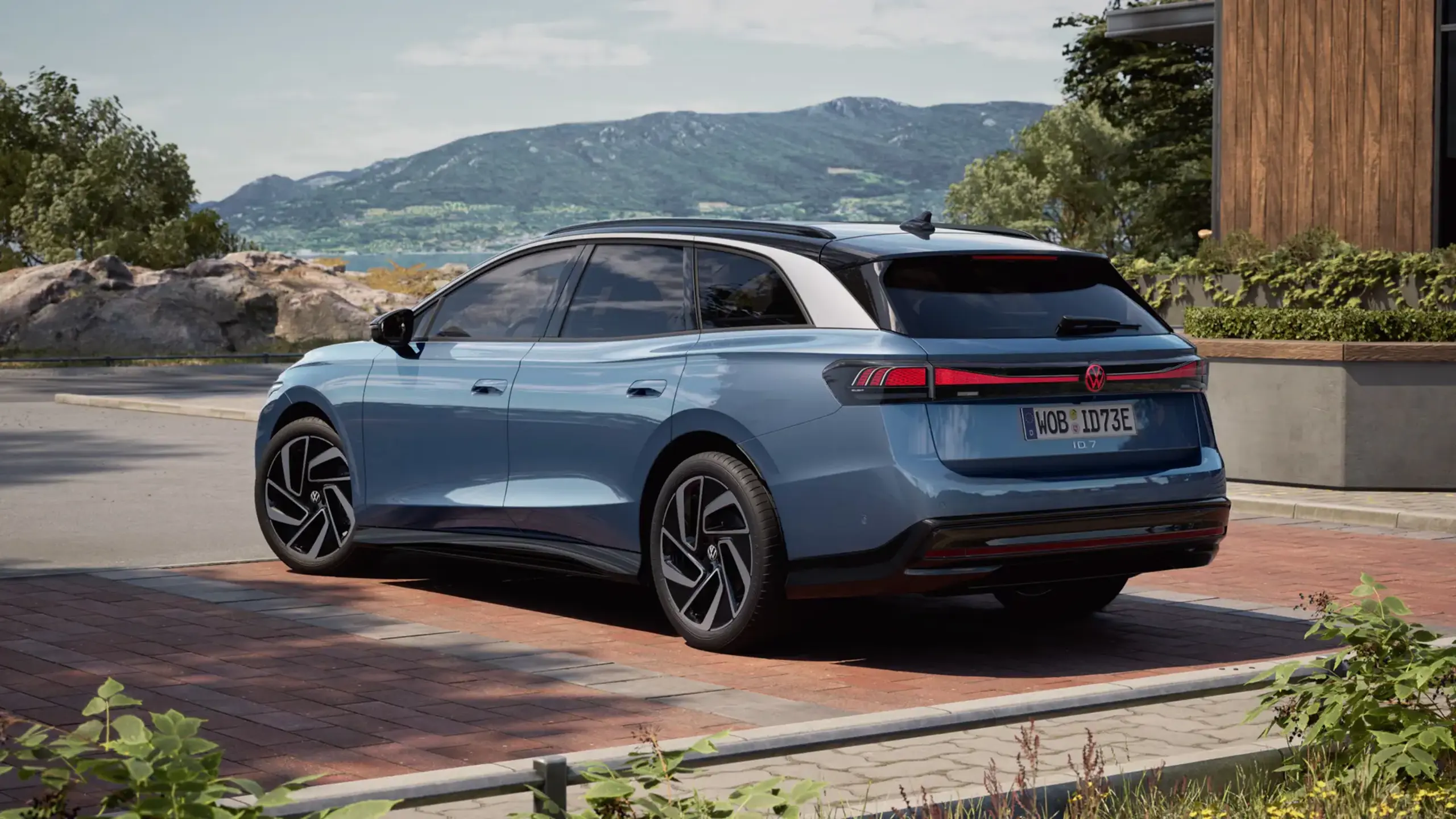 Blå ID.7 Tourer holder parkeret ved en hus med bjerge i baggrunden